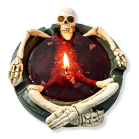 Thumbnail for Skeleton Halloween candle in dark green bowl filled with deep red wax, lit cotton wick glowing in center, sculptural skull and bone holder design, Maison De Flamme novelty decor candle