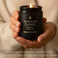 Thumbnail for Hand holding lit Maison De Flamme Apple & Cinnamon black jar candle — cozy warm apple spice home fragrance.